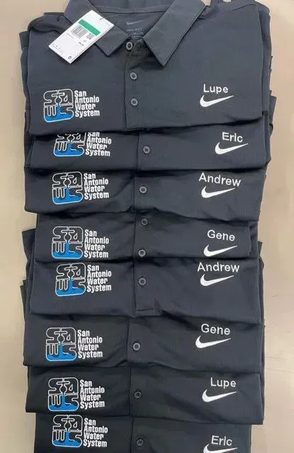 Pile of black Nike polo shirts with company logo and names.