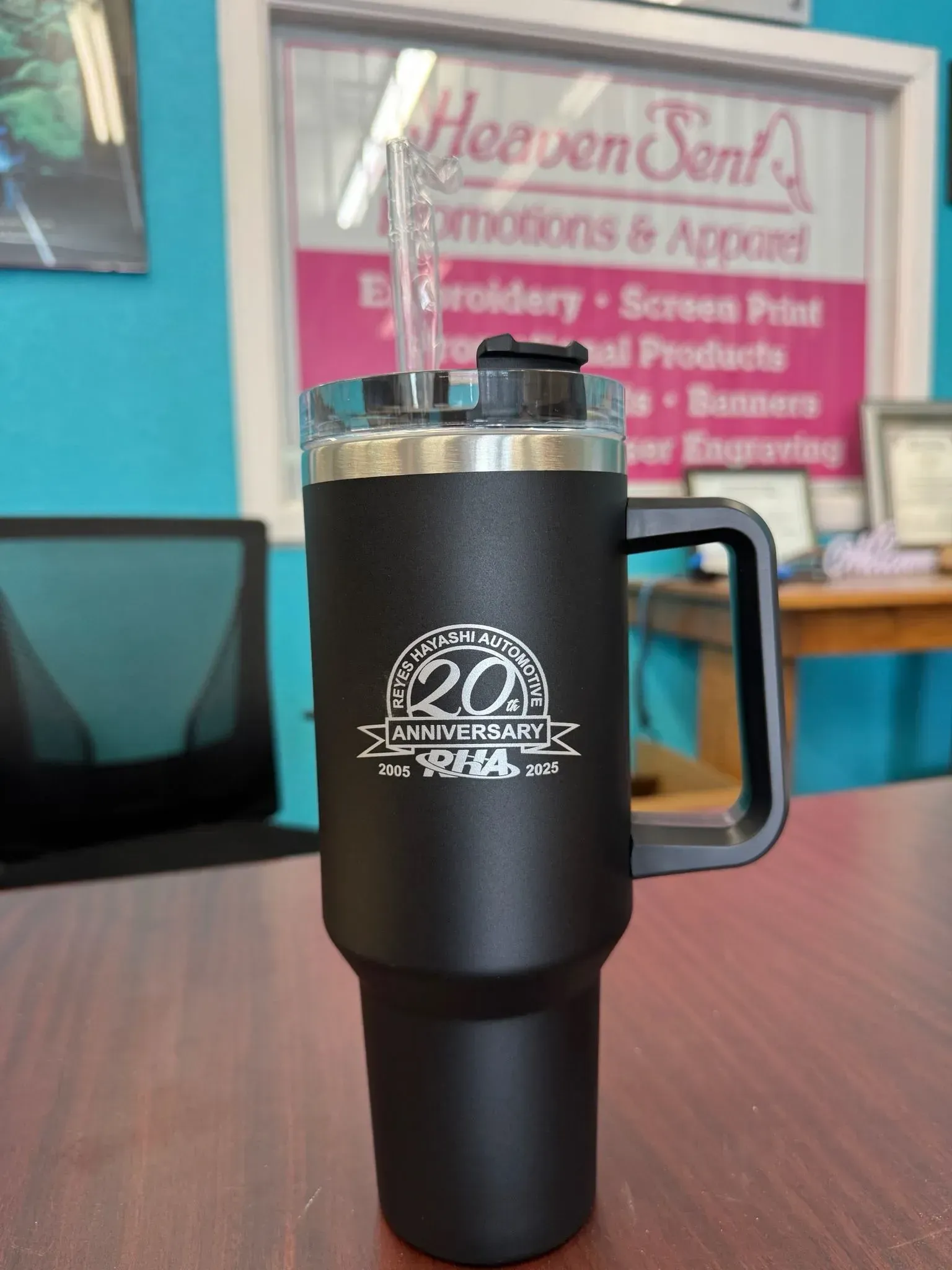 Black insulated tumbler with a handle, custom logo, and straw, on a table.