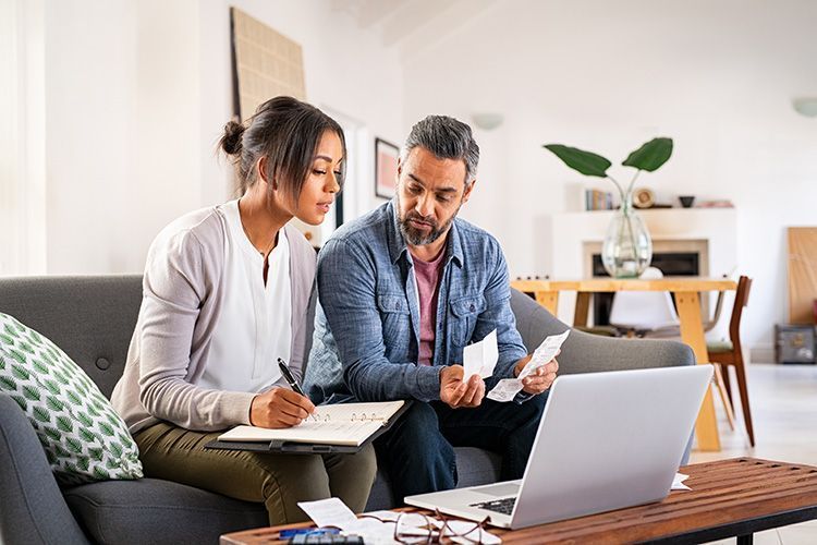 A man and a woman are sitting on a couch looking at a laptop.
