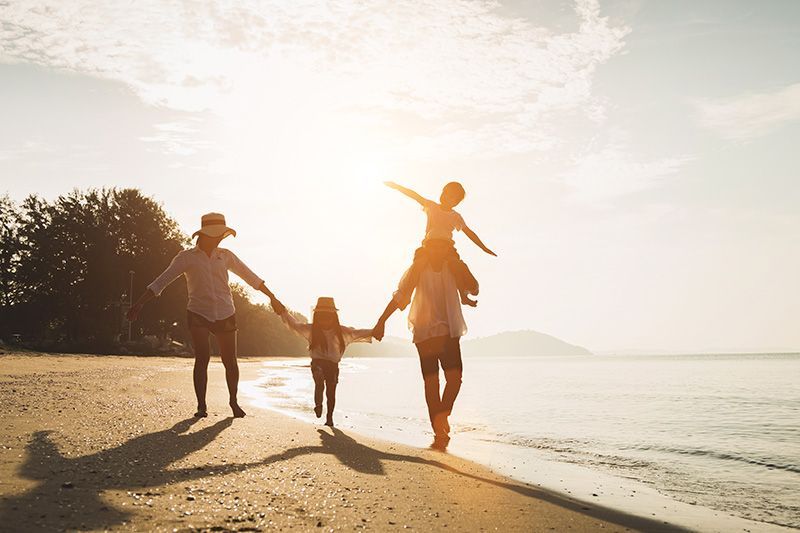 A family is walking on the beach at sunset holding hands.