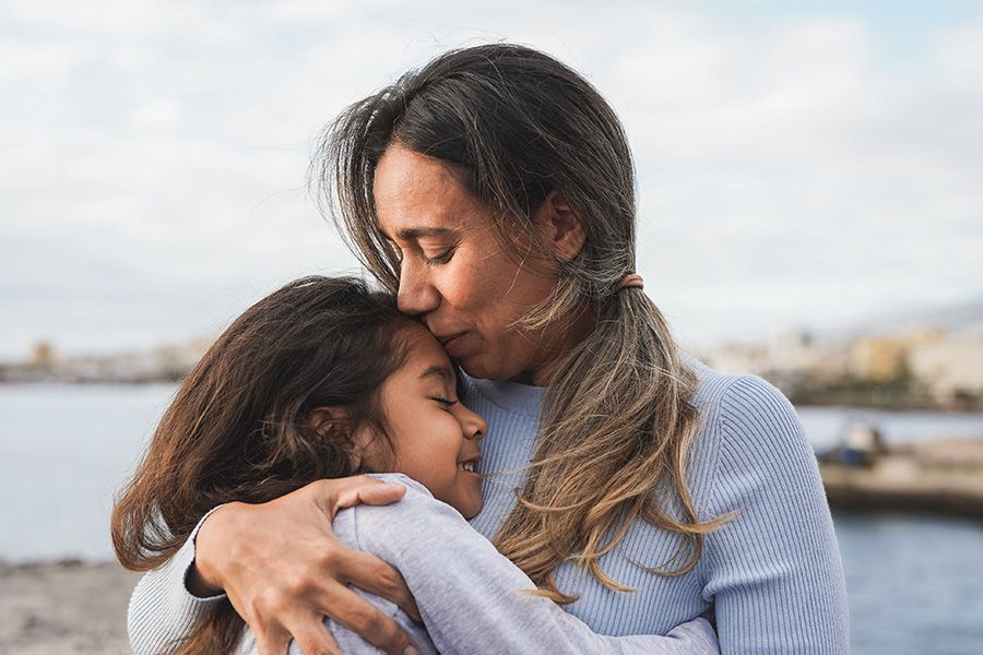 A woman is hugging a little girl on the beach.
