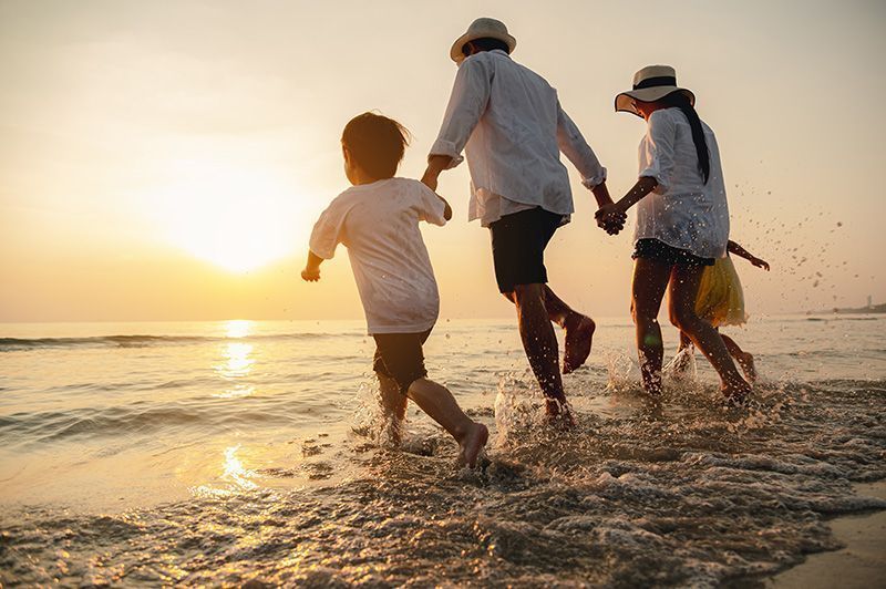A family is running on the beach at sunset.