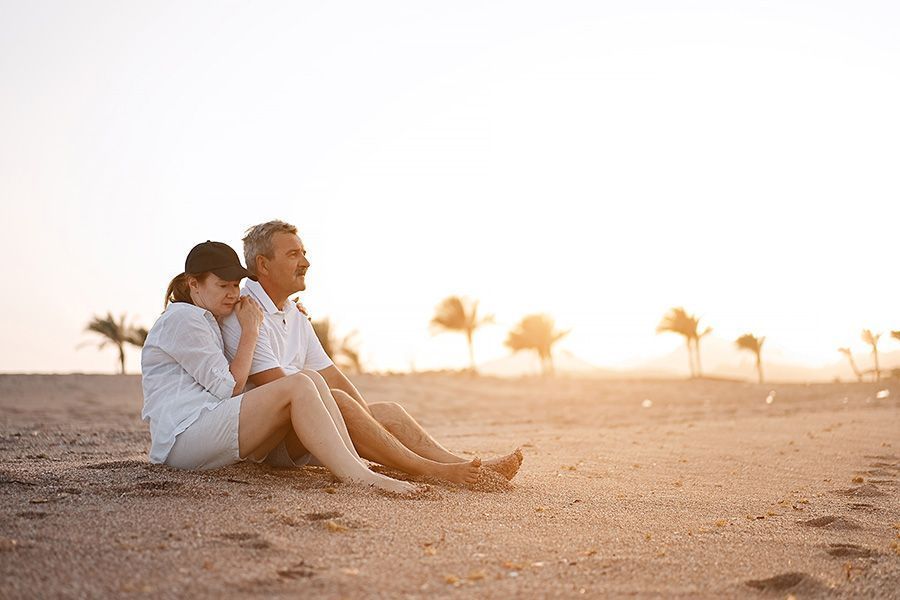 A man and a woman are sitting on the beach at sunset.
