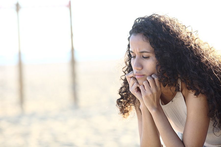A woman is sitting on the beach with her hands on her face.