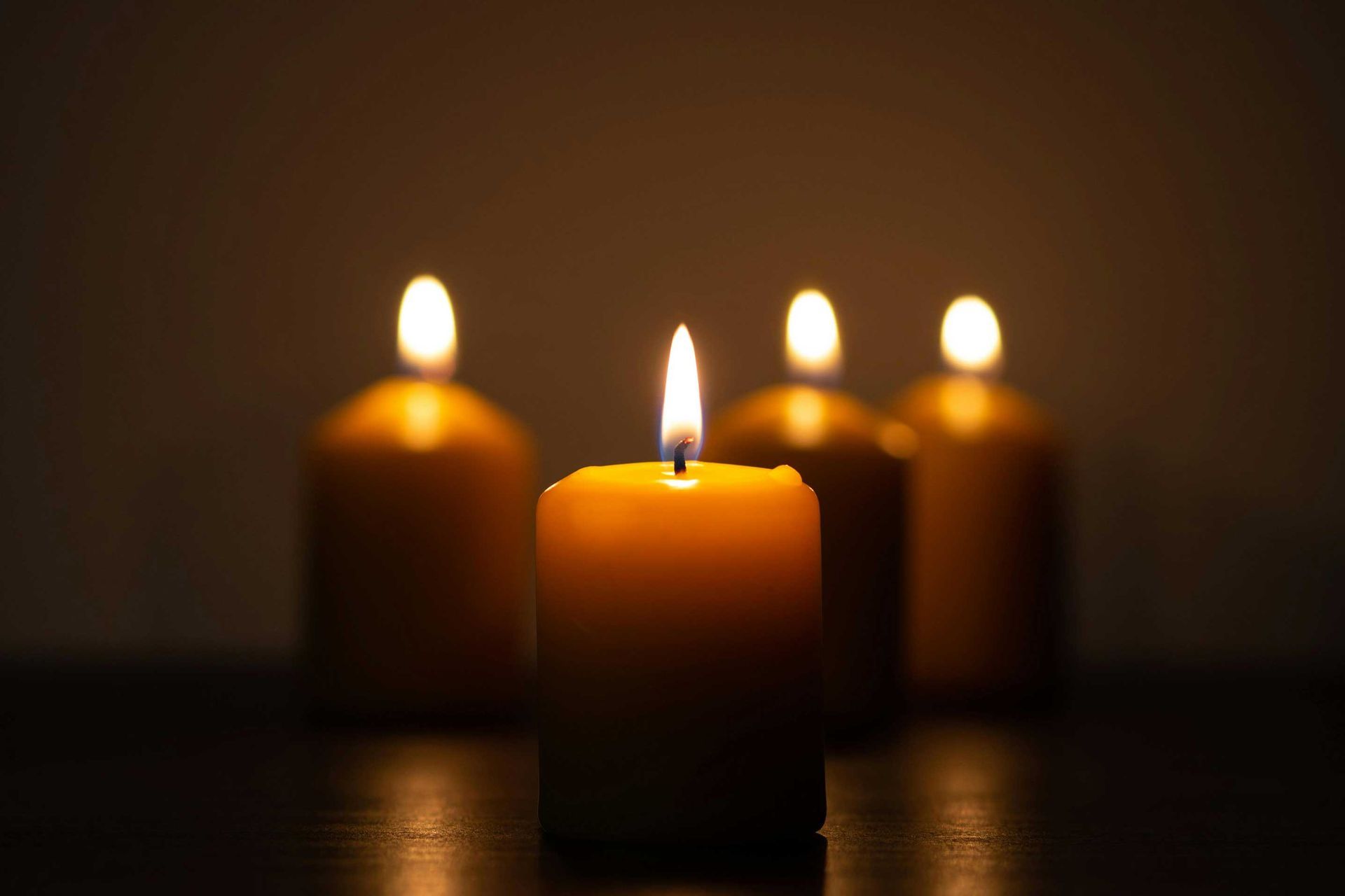 Three lit candles are sitting on a table in the dark.