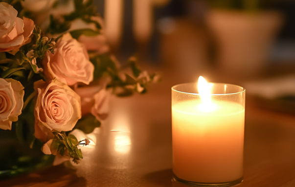 A lit candle is sitting on a table next to a vase of roses.