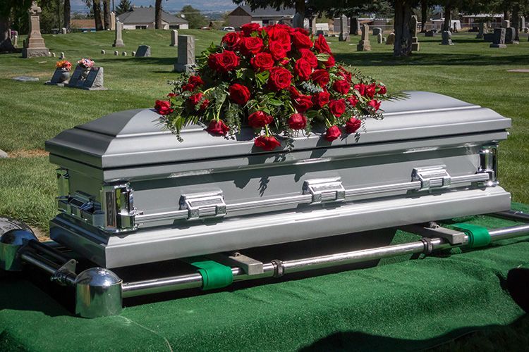 A silver coffin with red roses on top in a cemetery