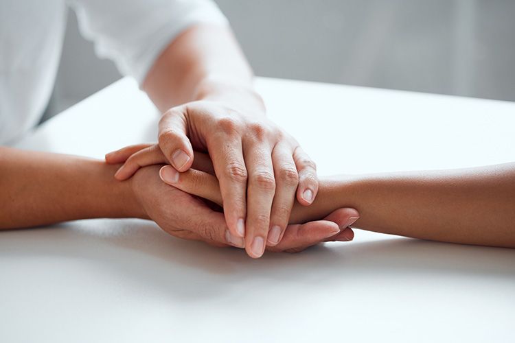 A person is holding another person 's hand while sitting at a table.