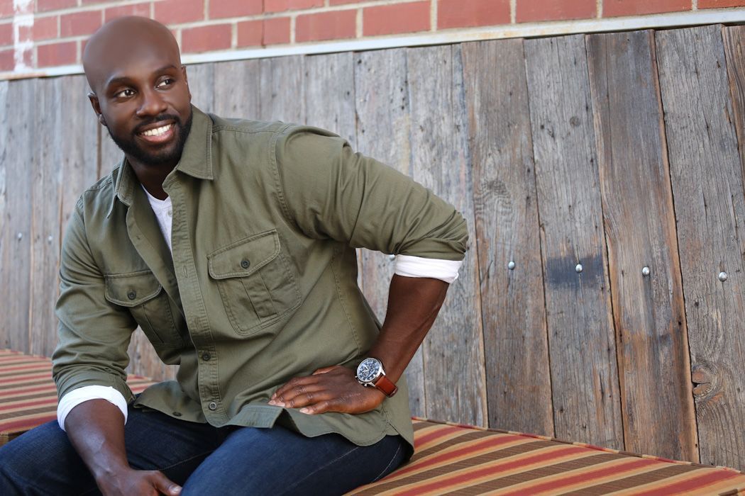 A Juntae Delane in a green shirt is sitting on a bench with his hands on his hips.