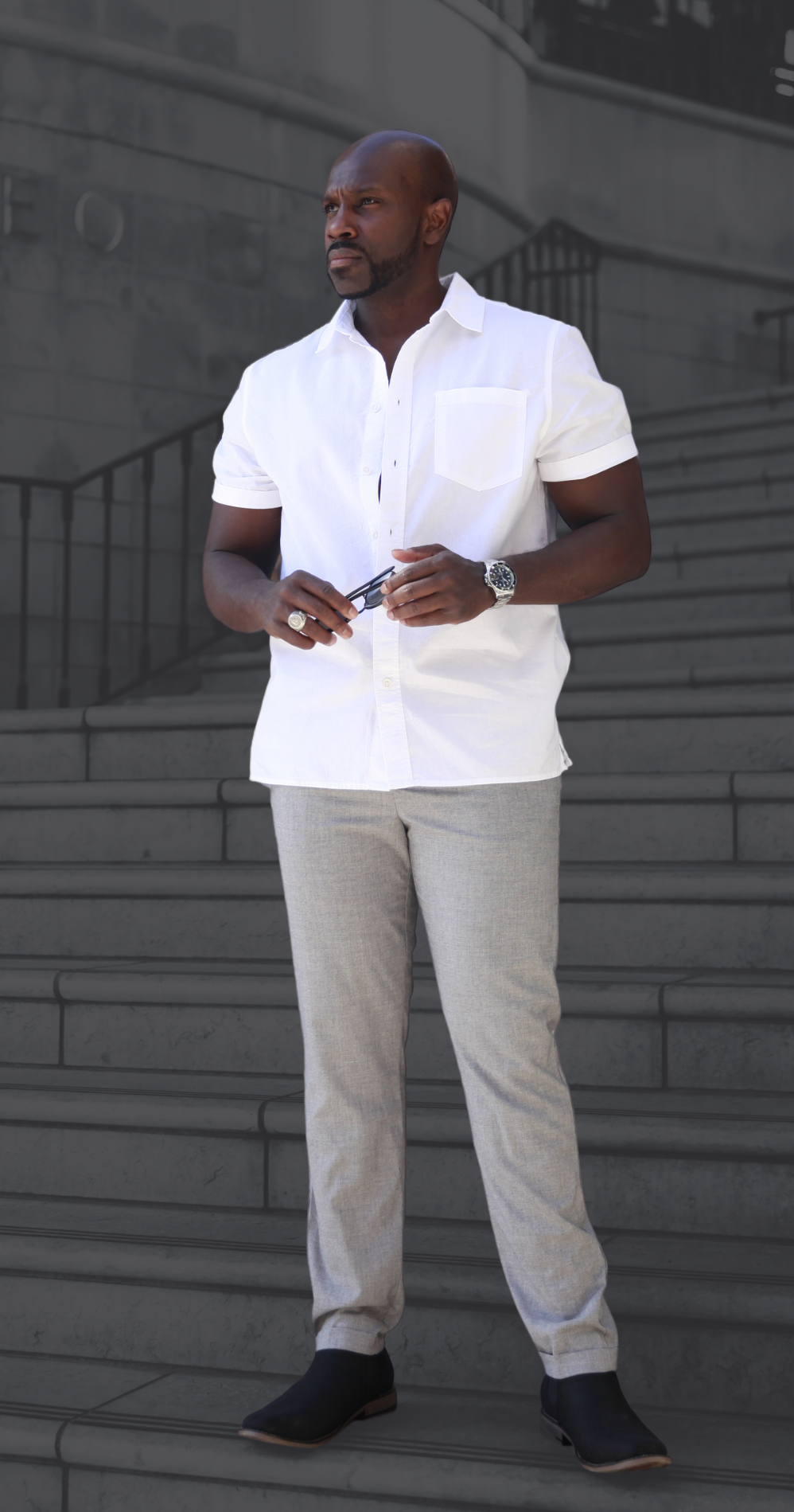 A man in a white shirt and grey pants is standing on a set of stairs.