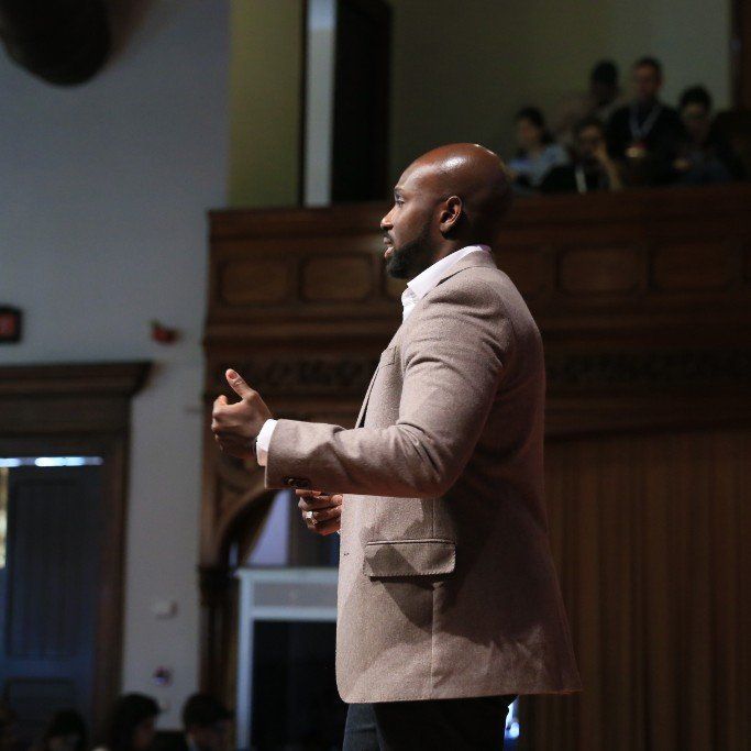 A Juntae Delane in a suit is giving a speech in front of a crowd.