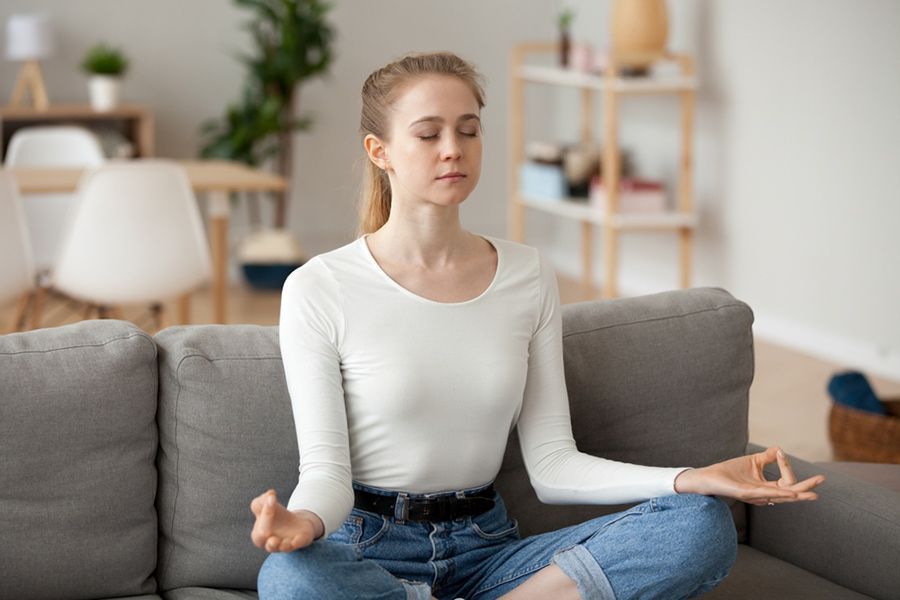 A Woman Is Sitting on A Couch in A Lotus Position with Her Eyes Closed — Align Health Therapies in Woonona, NSW