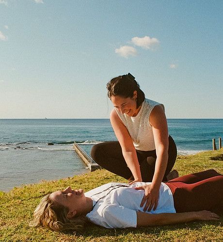 A Woman is Kneeling Over a Woman Laying on the Grass Near the Ocean — Align Health Therapies in Woonona, NSW