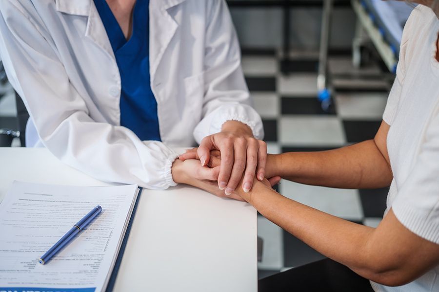 A Doctor Is Holding a Patient's Hand While Sitting at A Table — Align Health Therapies in Woonona, NSW