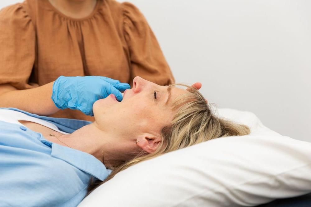 A Woman is Laying on a Bed While a Doctor Examines Her Neck — Align Health Therapies in Woonona, NSW