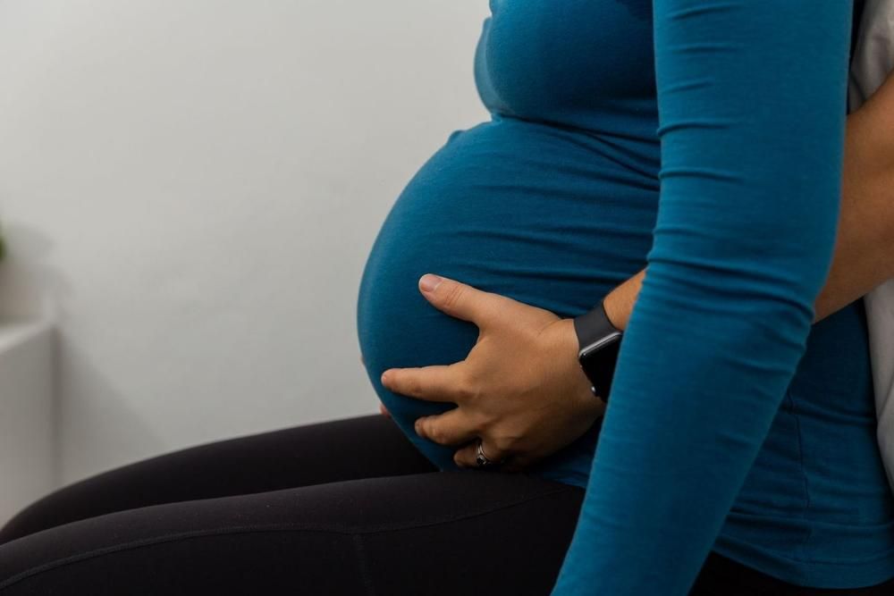 A Pregnant Woman in a Blue Shirt is Holding Her Belly — Align Health Therapies in Woonona, NSW