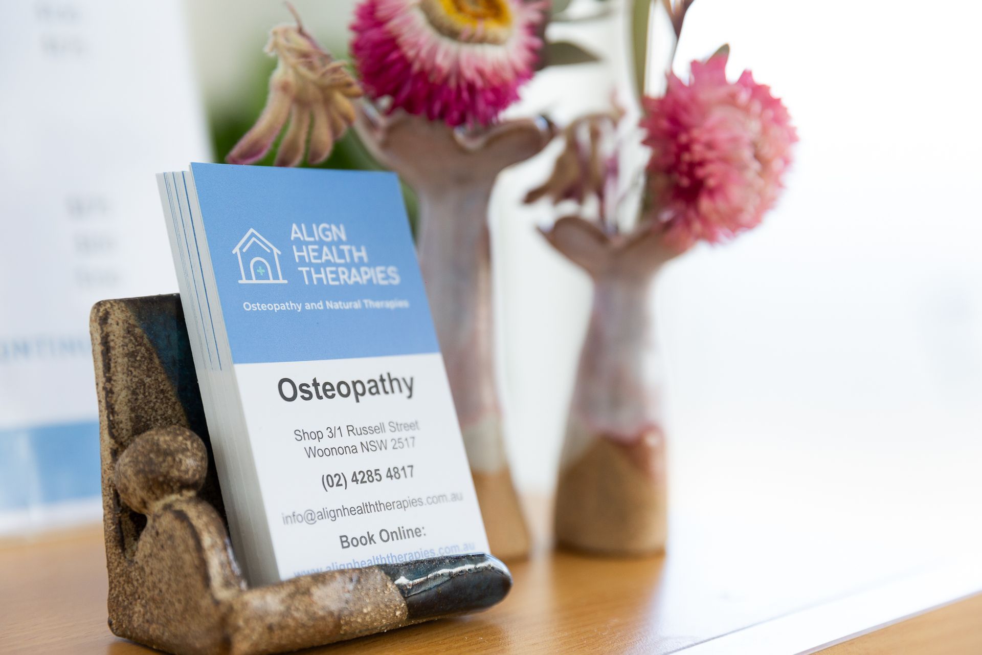 A business card is sitting on a table next to a vase of flowers — Align Health Therapies in Woonona, NSW