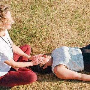 A Woman is Laying on the Grass While Another Woman Holds Her Hands Over Her Face — Align Health Therapies in Woonona, NSW