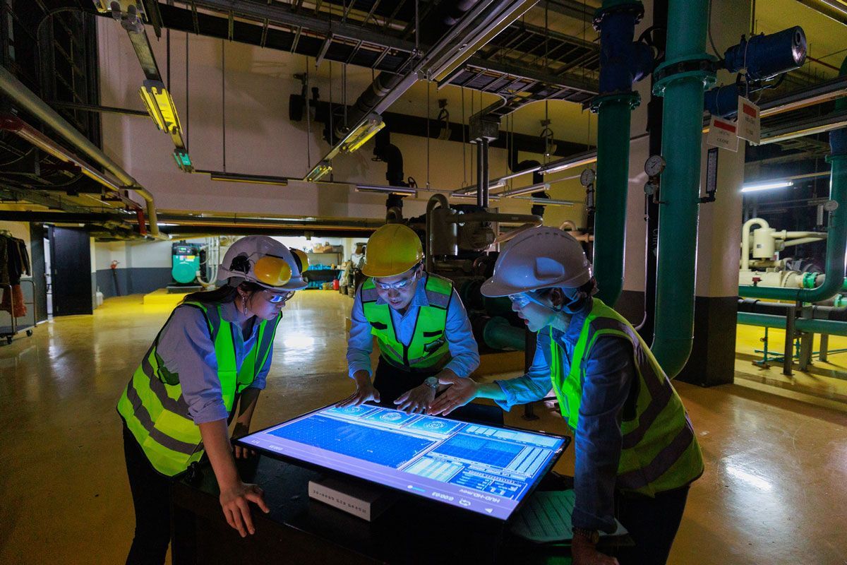 A group of construction workers are looking at a computer screen in a factory.