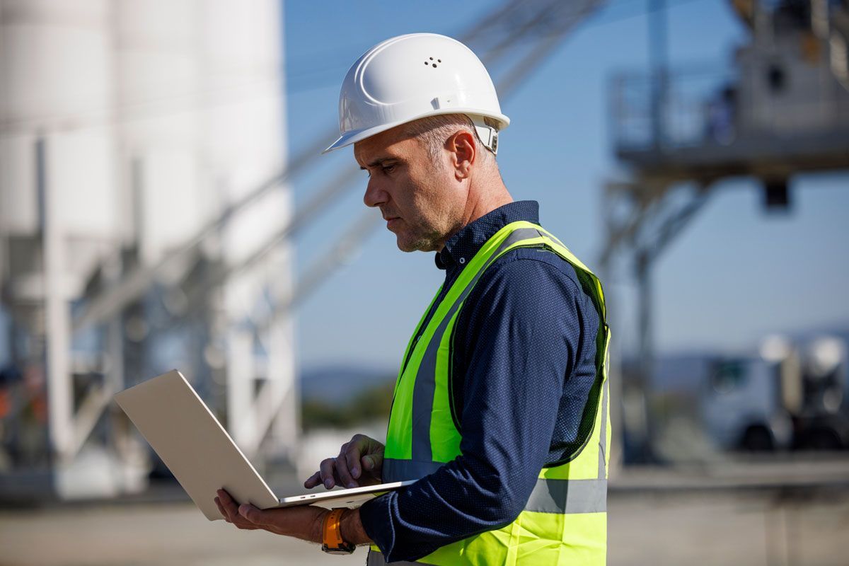 A man in a hard hat and safety vest is using a laptop computer.