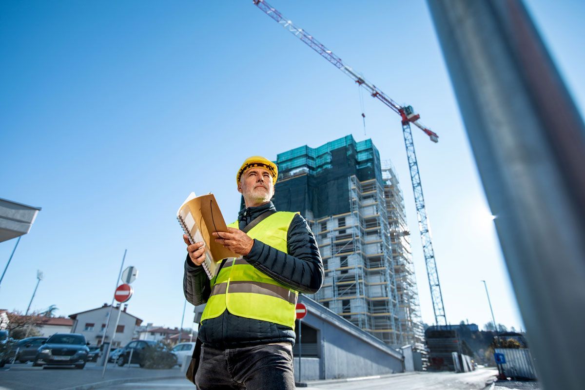 A construction worker is standing in front of a building under construction.