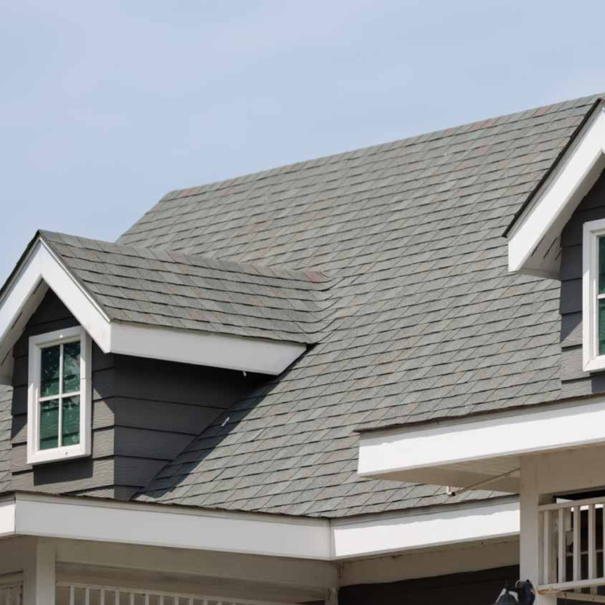 Gray shingled roof with two dormers, white trim, and blue sky.