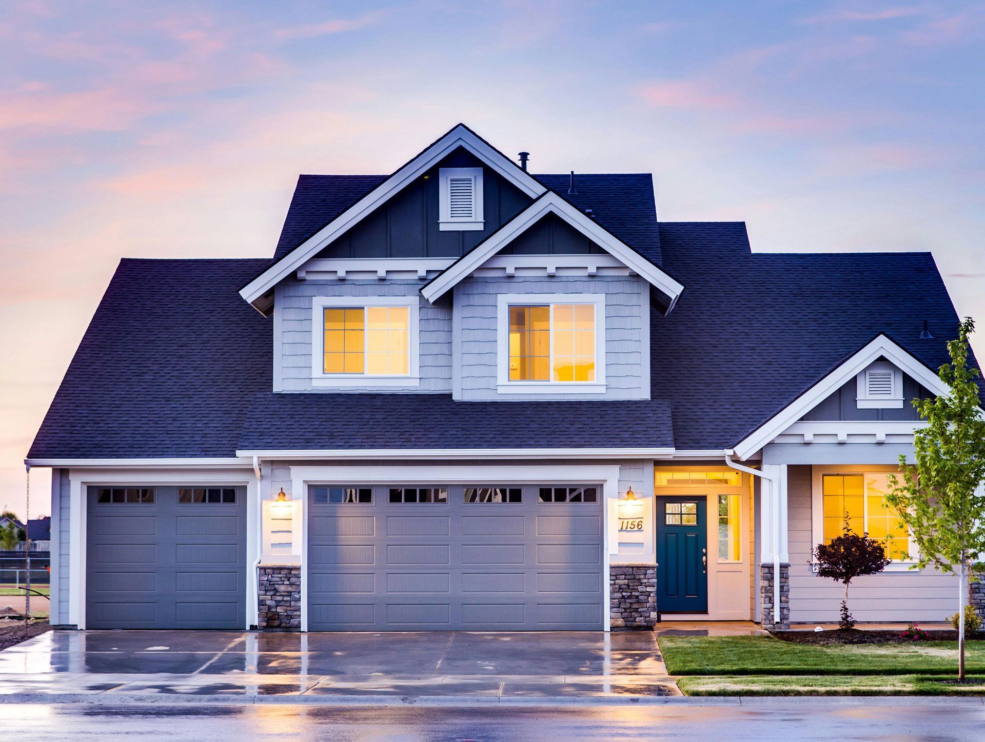 Two-story house with gray siding, dark roof, two-car garage, teal front door, and evening sky.