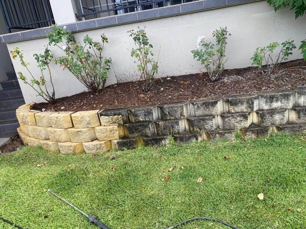 A Brick Wall In A Yard With A Hose Attached To It — Cap Coast Pressure Cleaning in Lammermoor, QLD
