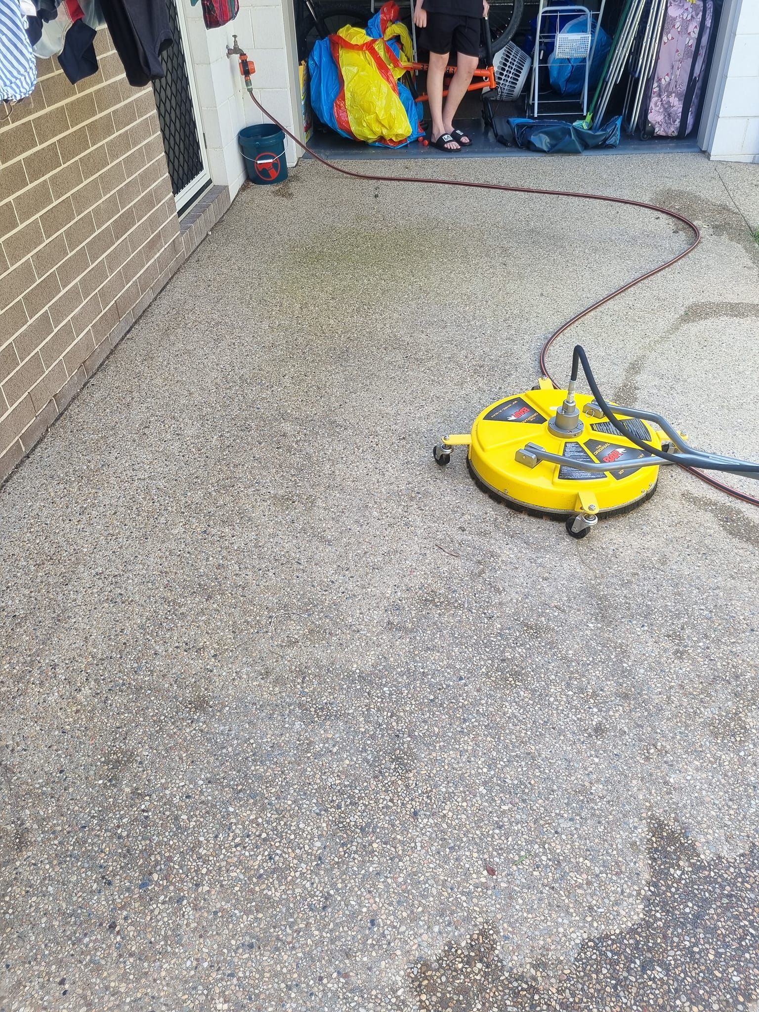 A Man Is Using A High Pressure Washer To Clean A Sidewalk — Cap Coast Pressure Cleaning in Lammermoor, QLD