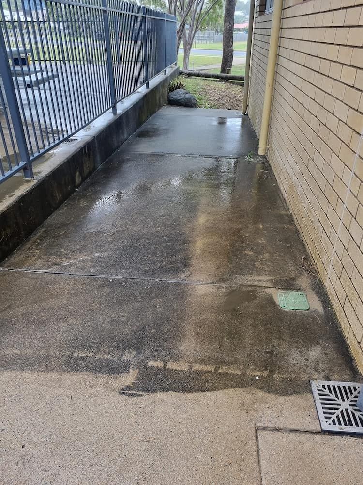A Concrete Walkway Next To A Brick Building With A Drain — Cap Coast Pressure Cleaning in Lammermoor, QLD