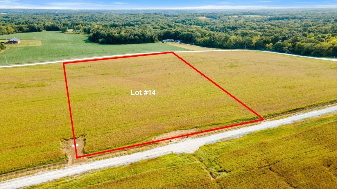 A grassy field bordered in red, next to a road and farmland.
