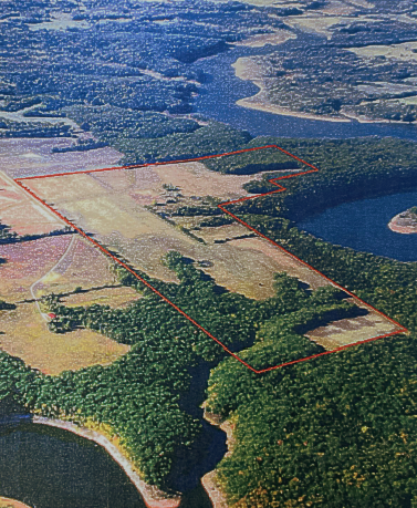 Aerial view of a field and forest with a river running through it, outlined in red.