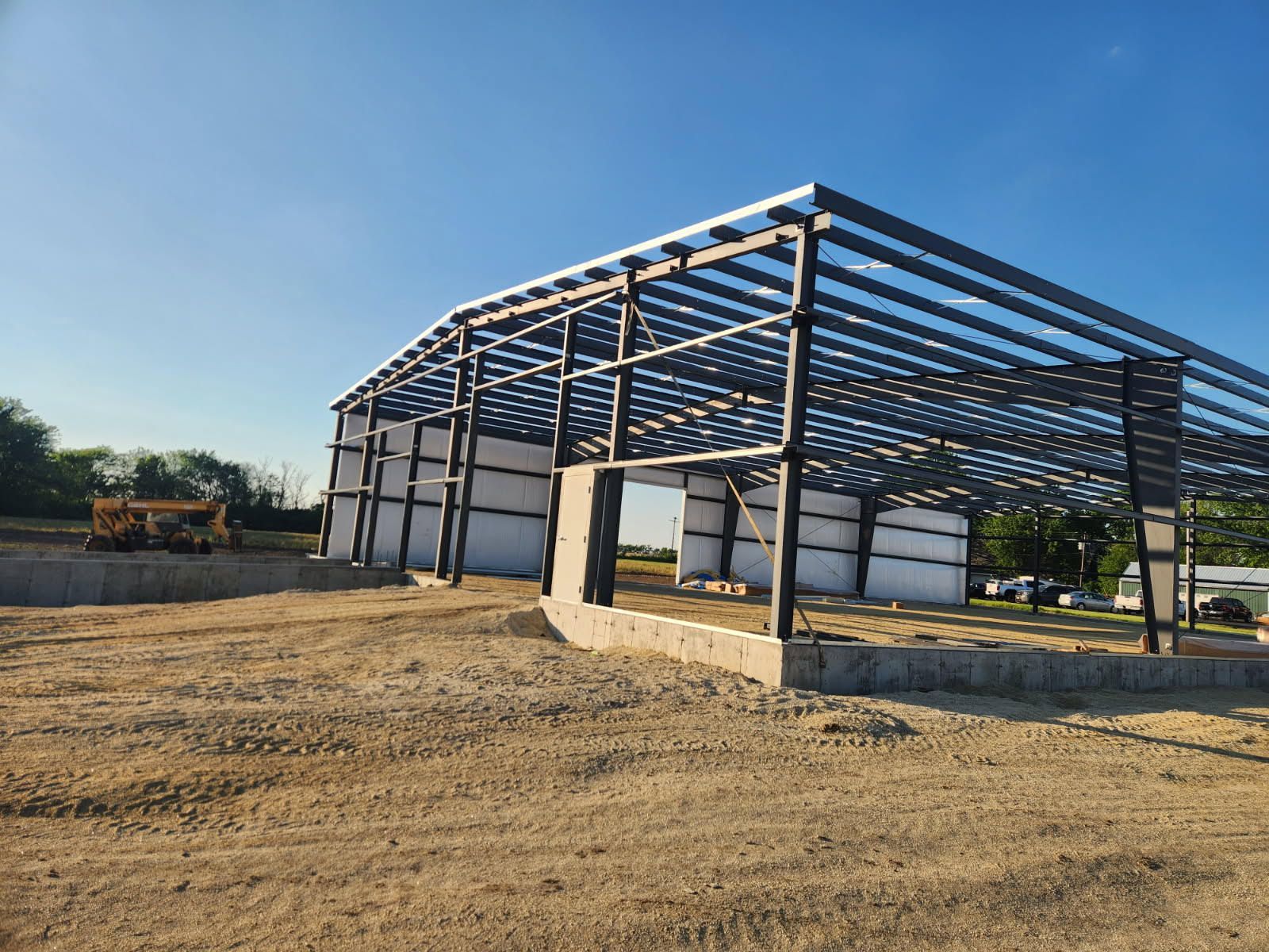 Steel frame of a new building under construction, set on a concrete foundation in a rural field.