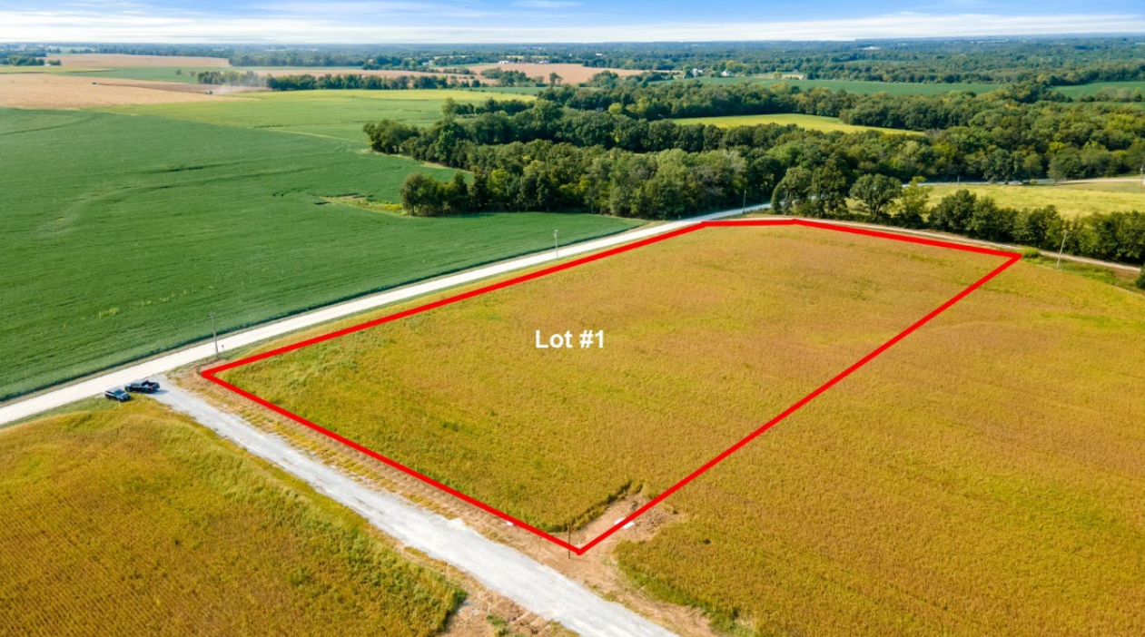 A grassy field bordered in red, next to a road and farmland.