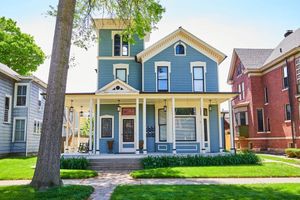 A blue house with a porch and a tree in front of it.