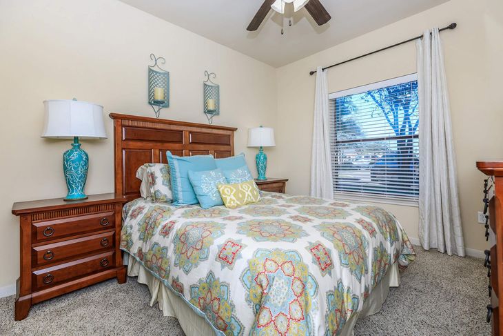 Bedroom with wooden furniture, patterned quilt, turquoise lamps, and window with sheer curtains.