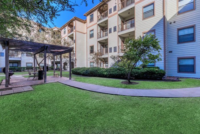 Apartment complex exterior with pergola, green lawn, and walkways.