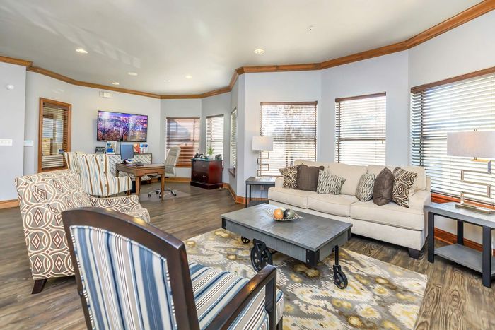 Lobby with seating: patterned armchairs, sofa with decorative pillows, coffee table, desk area, and windows.