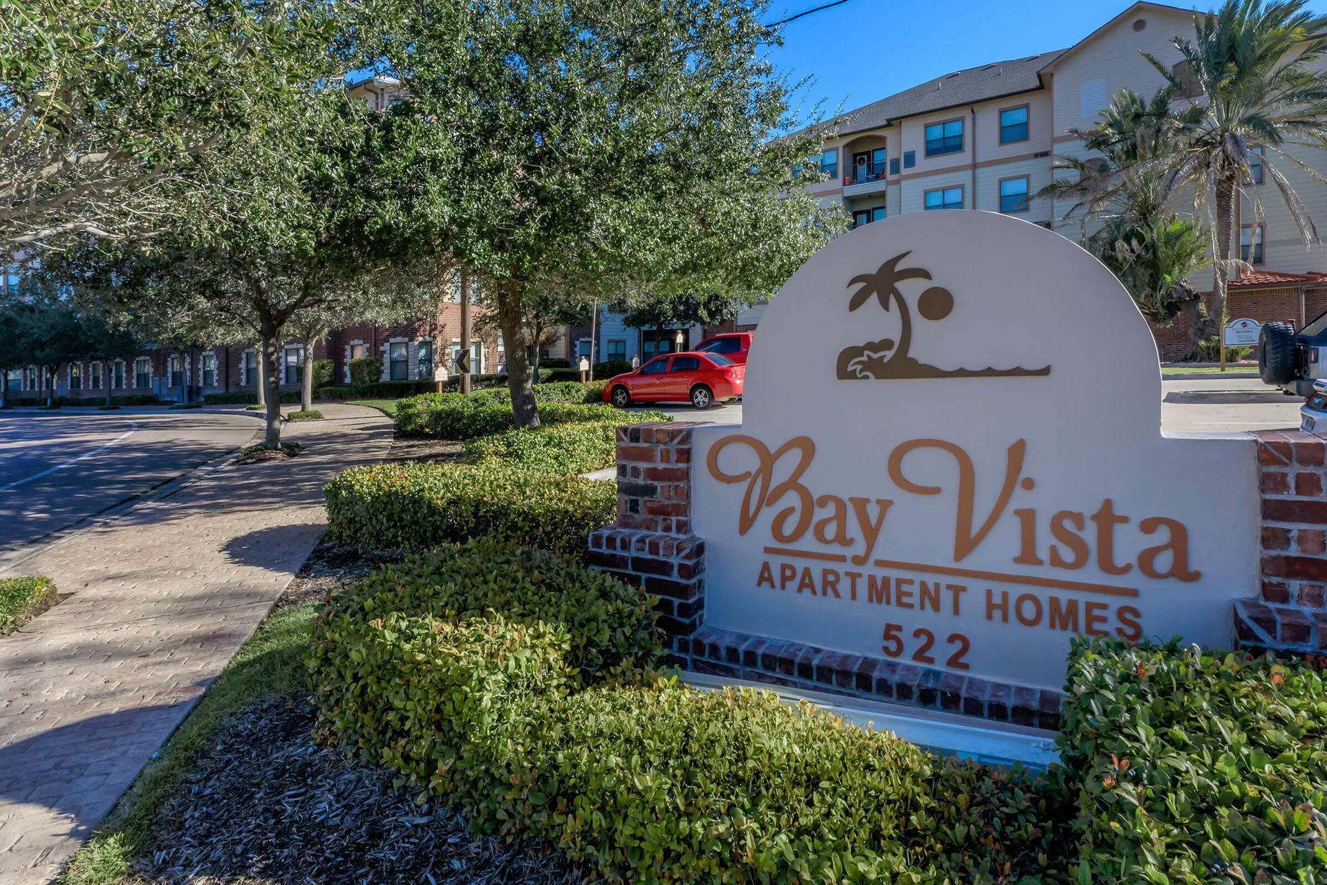 Bay Vista Apartment Homes sign with logo, 522 address. Trees and building in background.