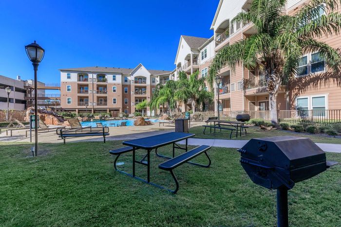 Picnic area with tables, grill, and apartment buildings under a blue sky.