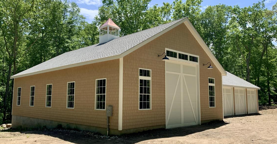 A large barn with white doors and windows is surrounded by trees.