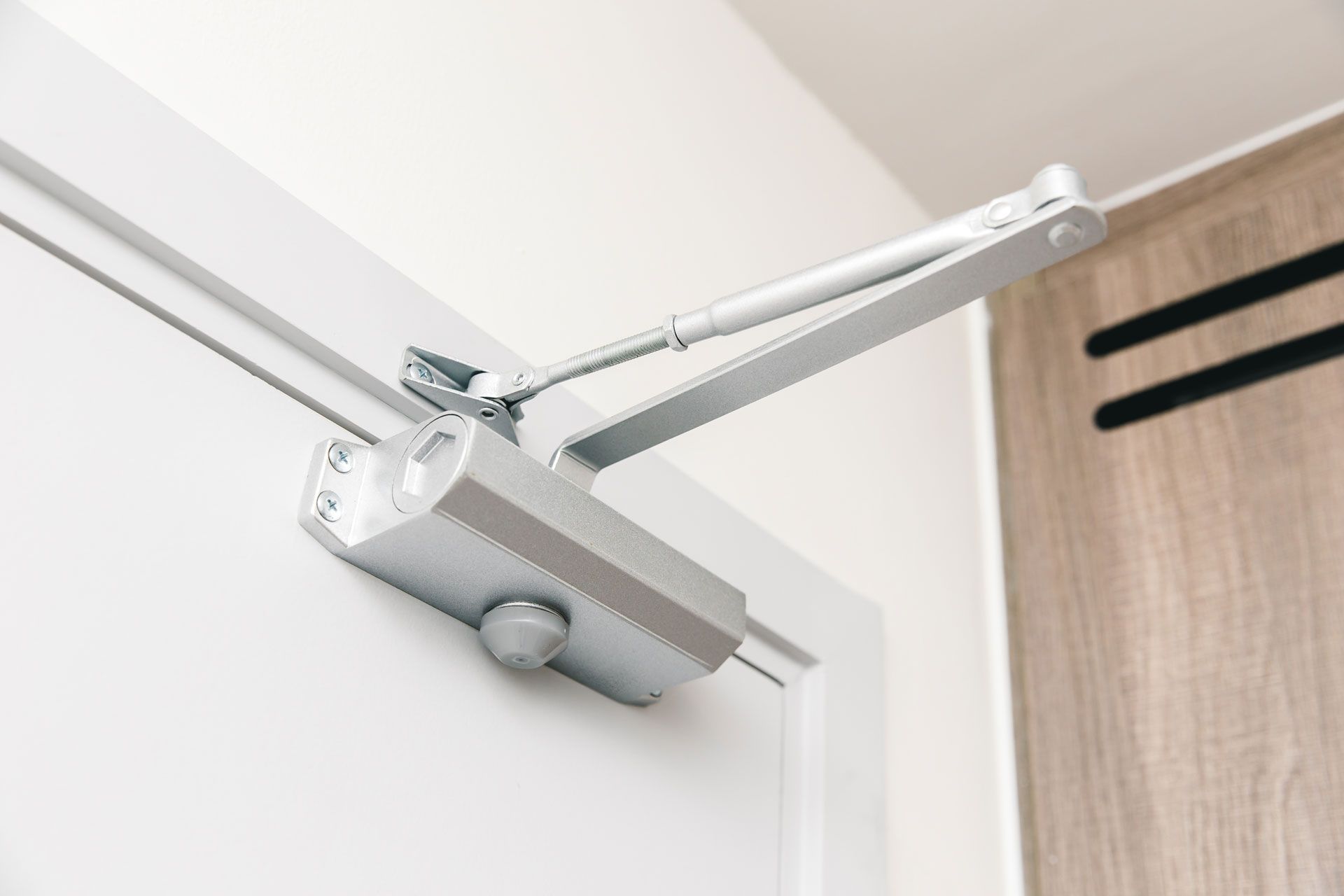 A close up of a door closer on a white door.