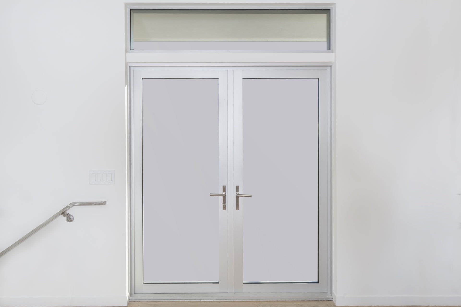 A pair of white doors with a handrail next to them on a white wall.