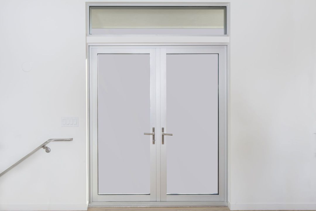 A pair of white doors with a handrail next to them on a white wall.