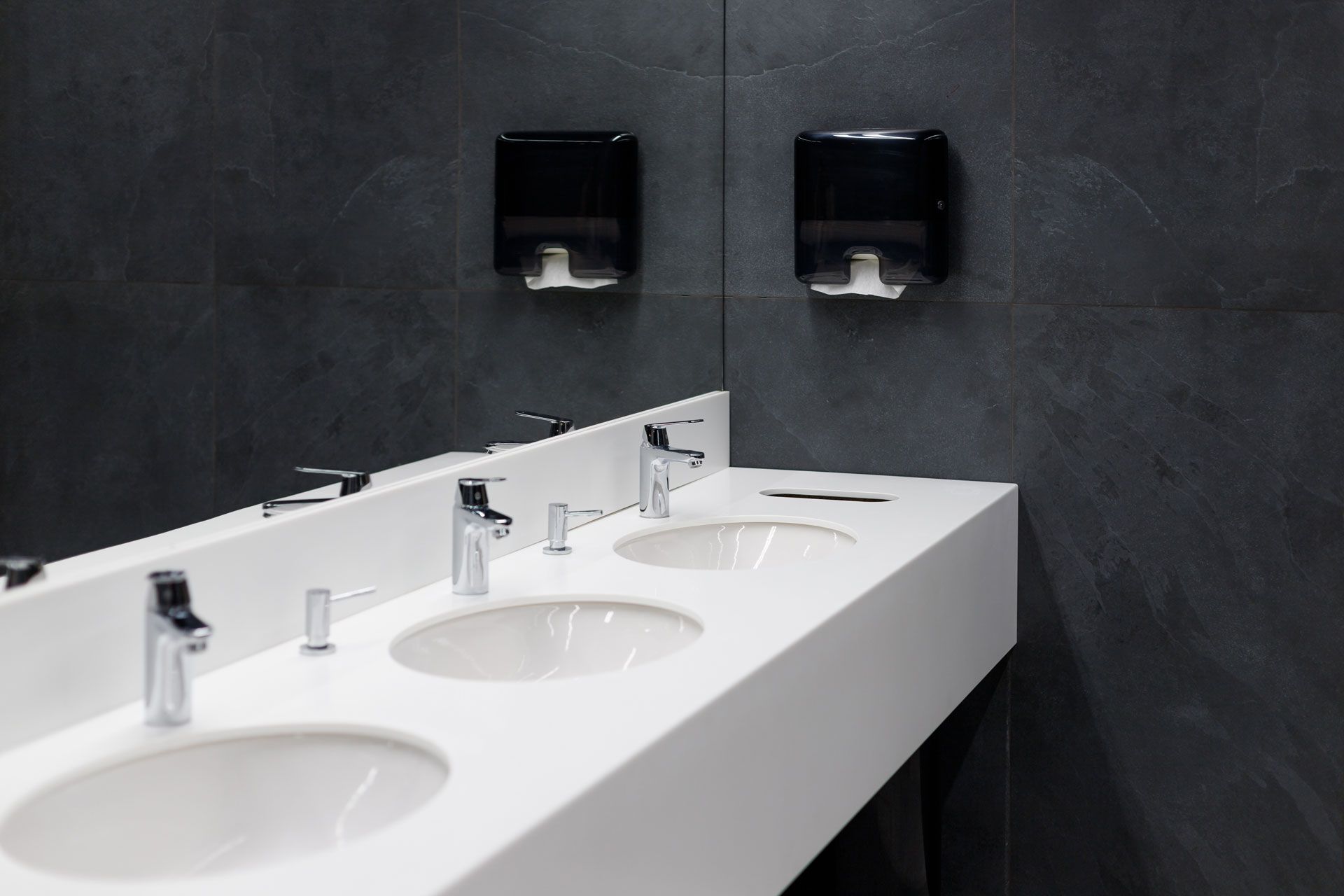 A bathroom with three sinks and two paper towel dispensers