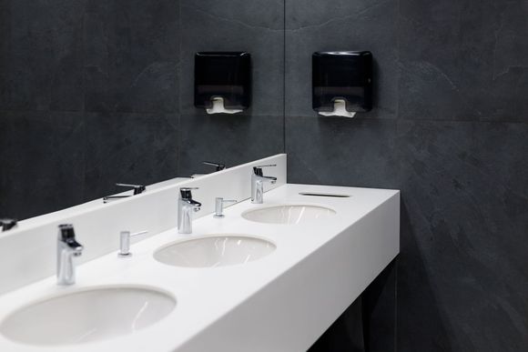 A bathroom with three sinks and two paper towel dispensers