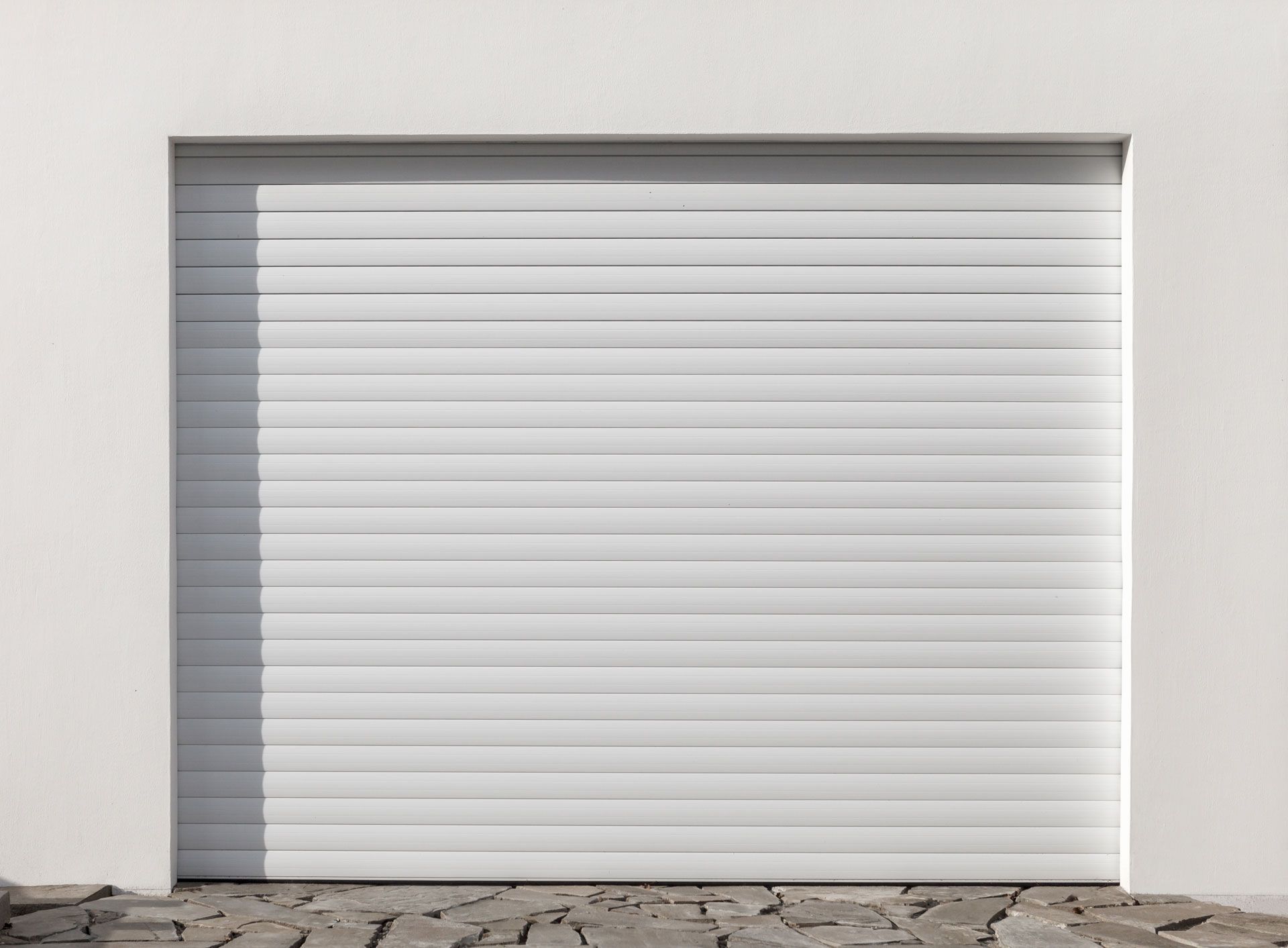 A white garage door is sitting on the side of a white building.