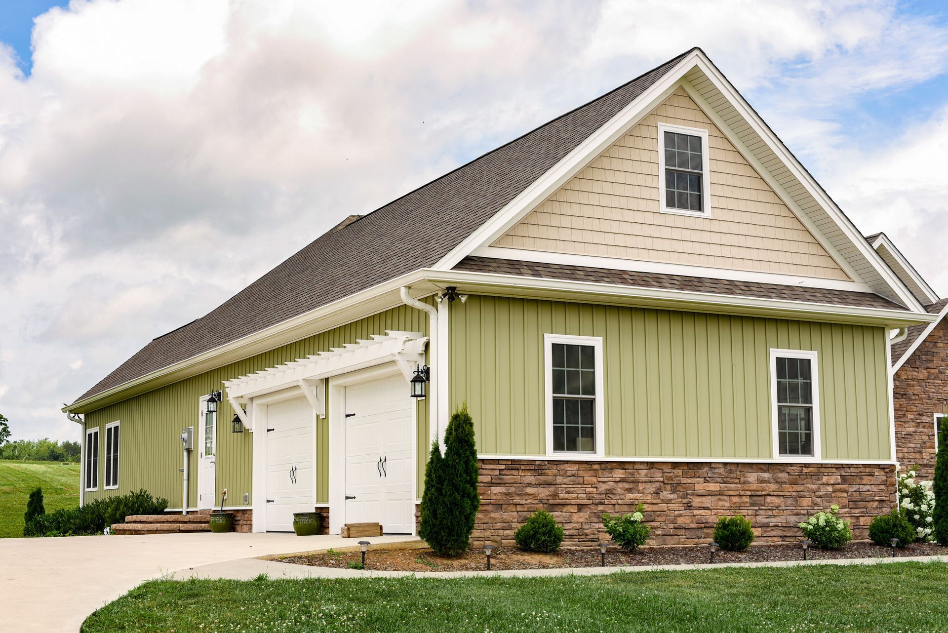 A green house with two garage doors and a stone wall.