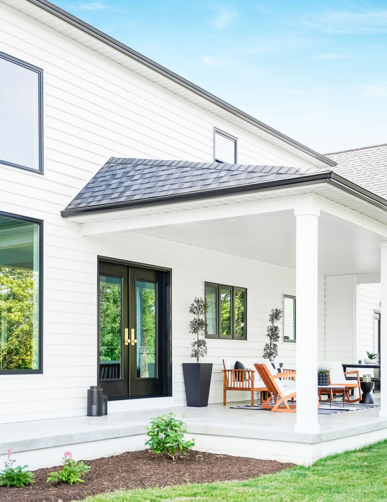 A white house with a large porch and a black roof.