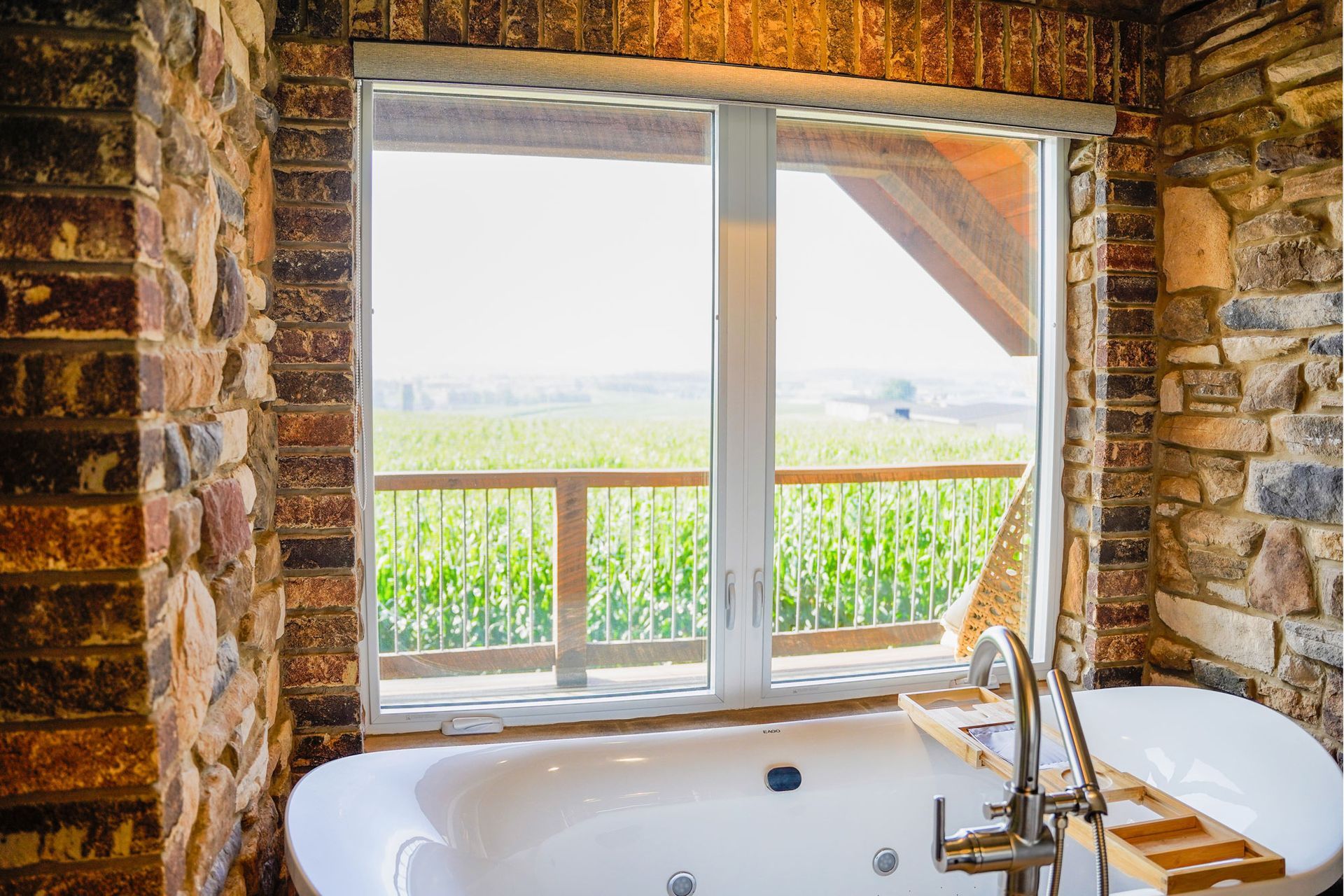 A bathroom with a tub and a window with a view of a corn field.